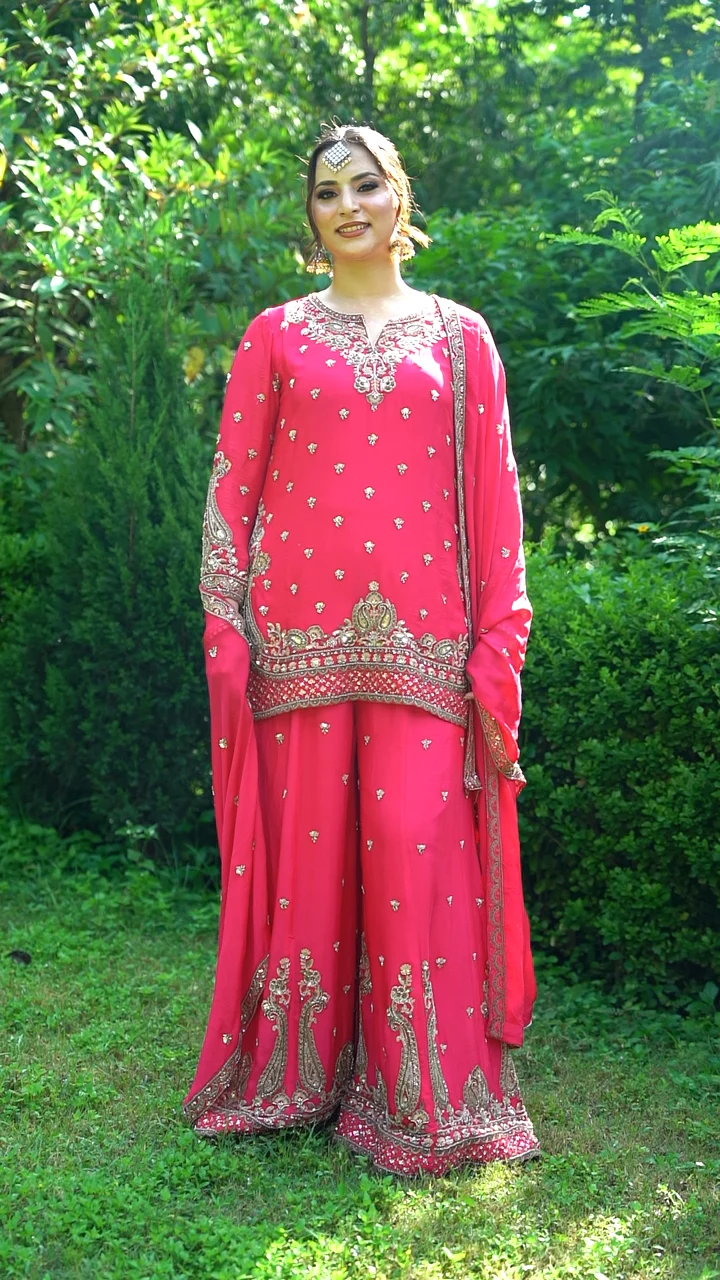 Fuchsia embroidered suit filmed outdoors as the model walks and lifts the dupatta